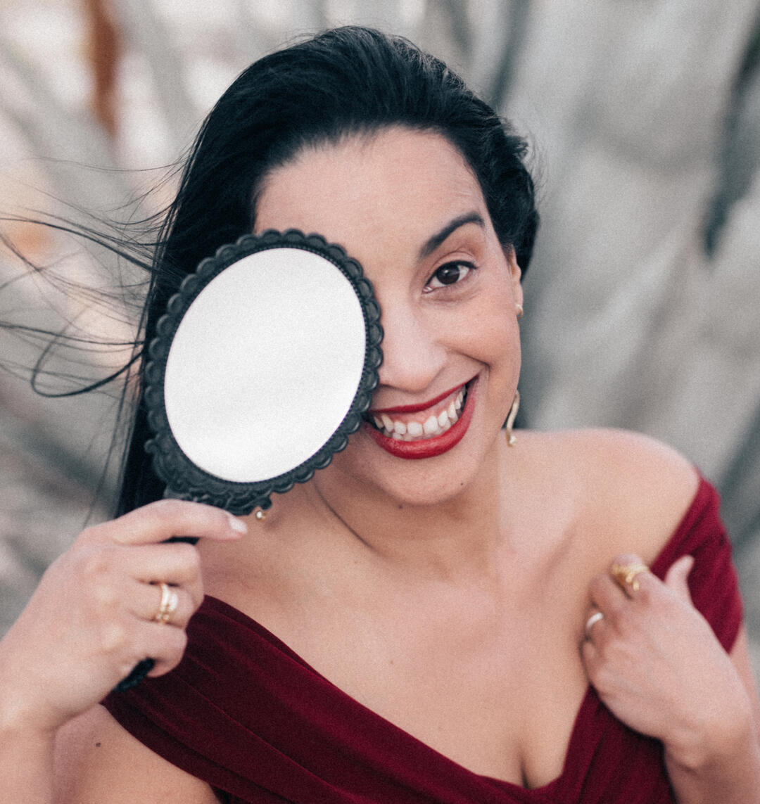 Meet Jessy Furniel, Mentor for Bad Bitches with Big Heart Jessy Furniel holding a mirror to you at Joshua Tree with dessert background and red lipstick.